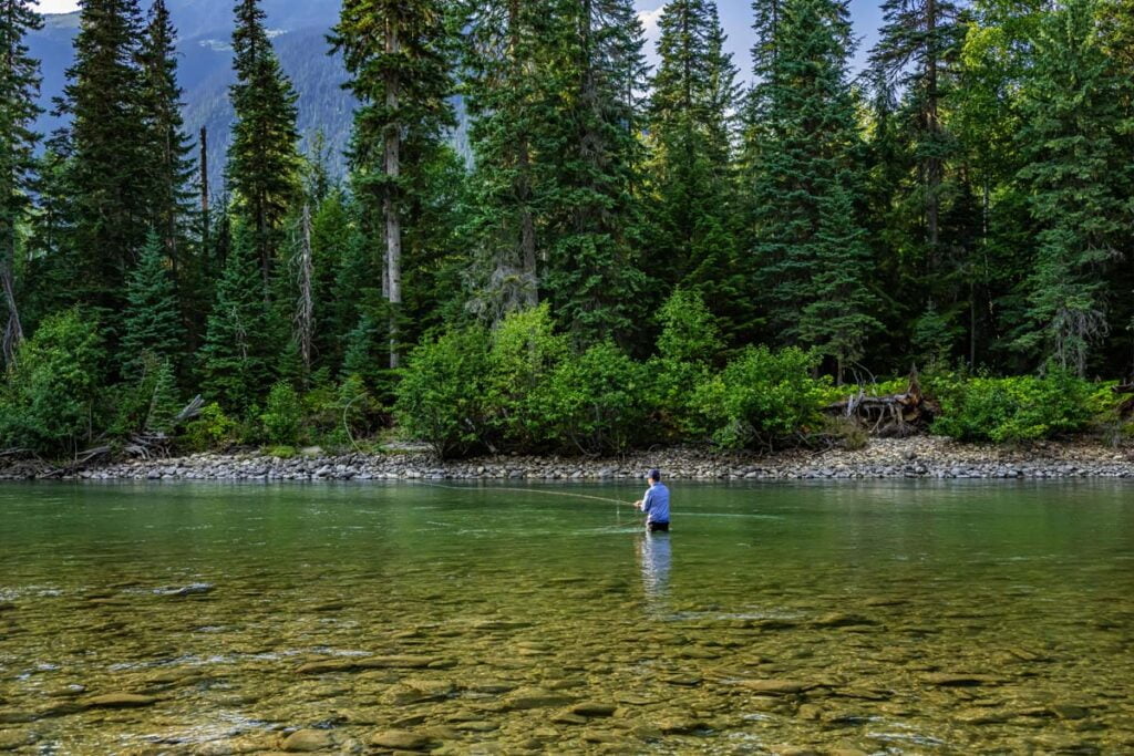 angler casting fly rod on remote freestone river in British Columbia wilderness